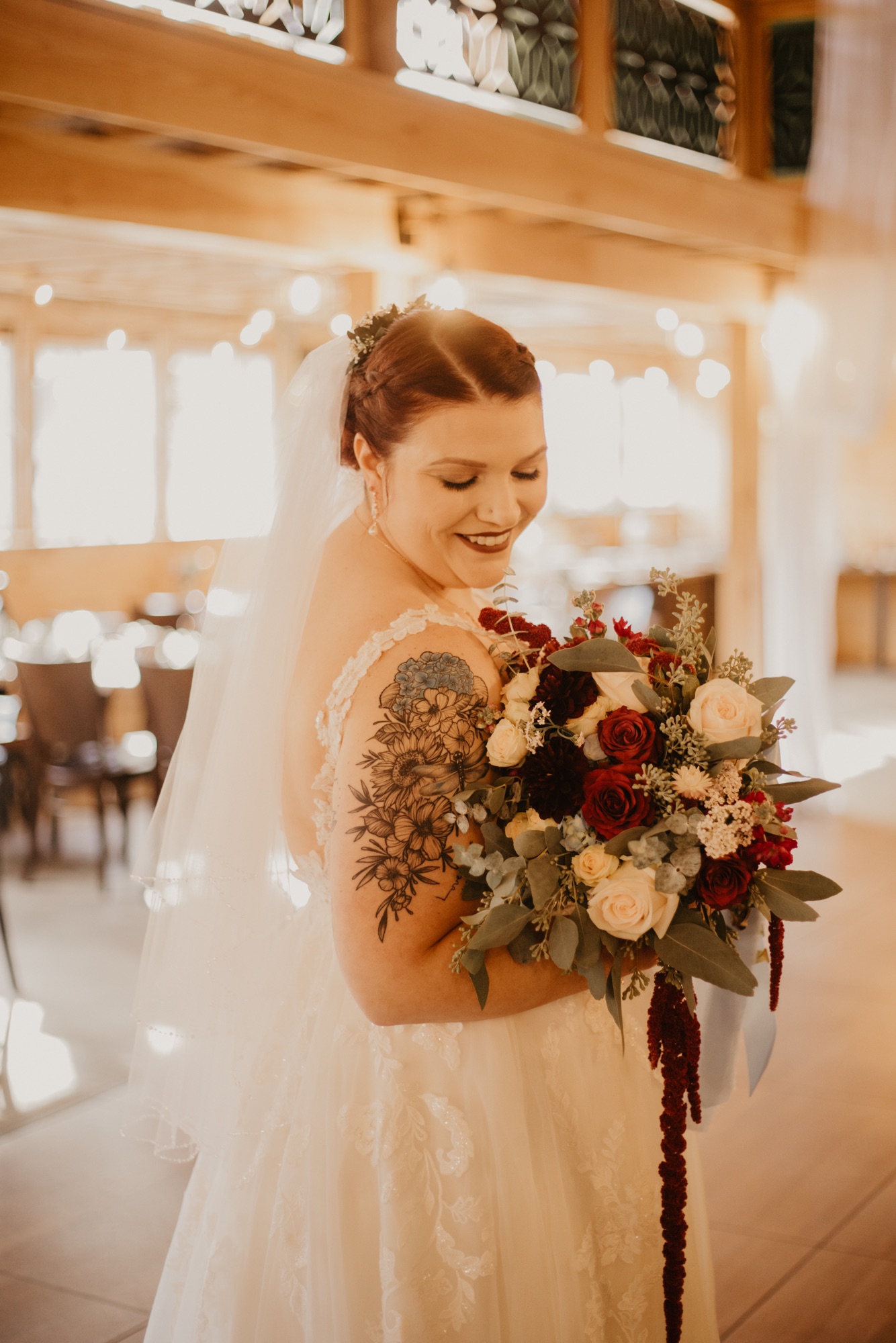 Bride in a fitted lace wedding gown holding a fall bouquet while standing outdoors with long veil trailing. Dress from Blue Violet Bridal Prom & Tux serving brides in CT and RI.